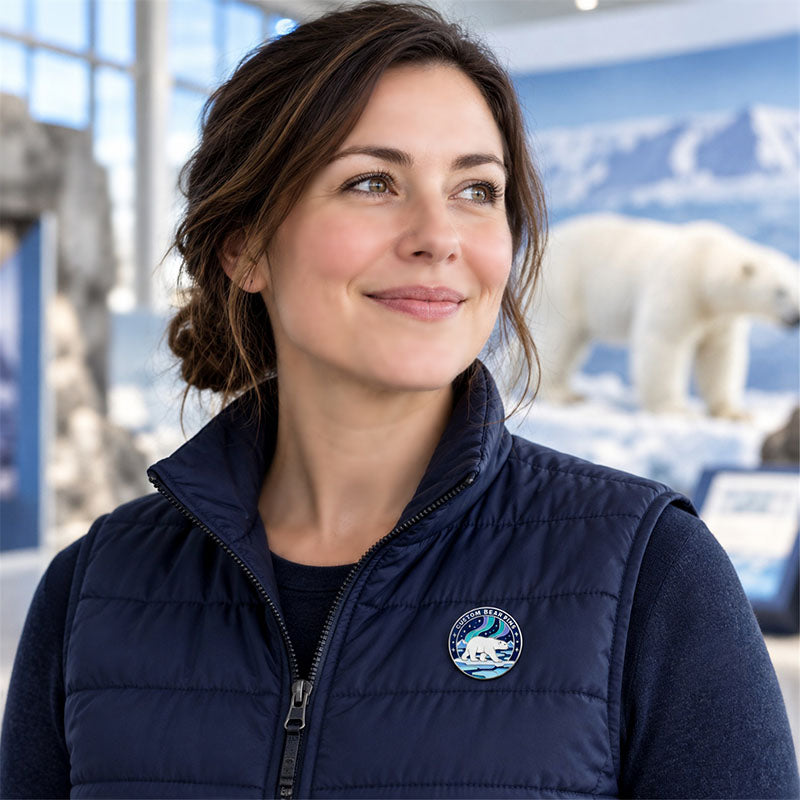 Woman wearing a round polar bear enamel pin on a navy vest beside a polar bear display