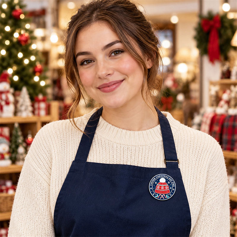 Woman wearing a round Christmas hat pin on a navy apron inside a decorated holiday shop