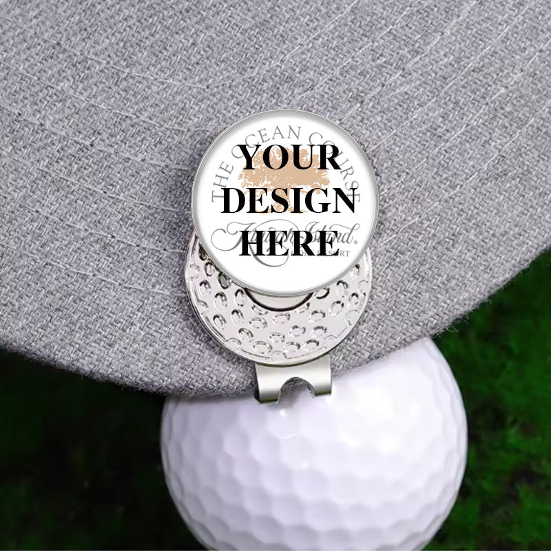 custom golf ball marker hat clip with custom text areas and decorative inscriptions, attached to a gray hat brim with a white golf ball against a blurred green golf course background