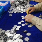 Skilled factory worker meticulously installing butterfly clutches and performing 100% manual inspection on finished custom pins, before final packing for shipment