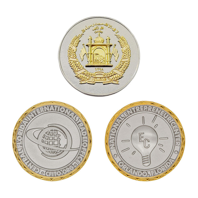 Three custom two-tone plating coins in gold and silver, featuring designs of a building, orbiting Earth, and a lightbulb, with custom text including Arabic script and organizational names.