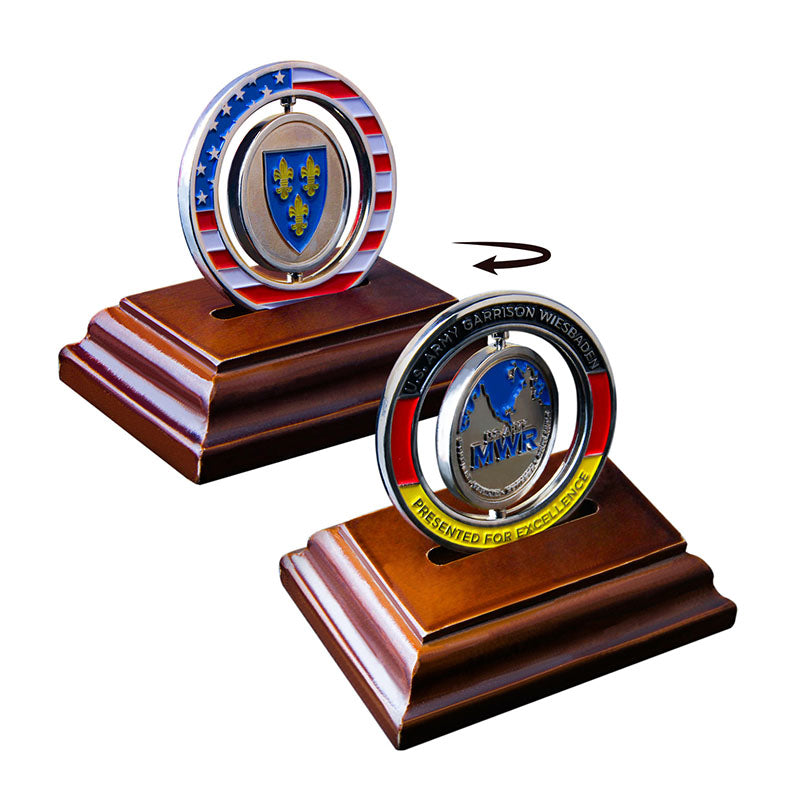 Spinner challenge coins on wooden bases. Front silver coin features 'MWR' and military text, rotating to show a blue shield coin with fleur-de-lis and star-stripe border.