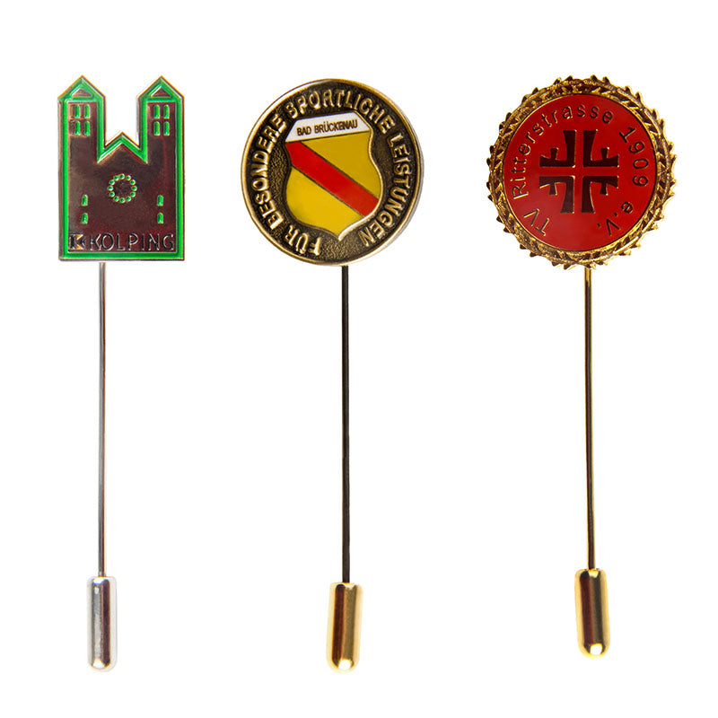 Three designs of custom stick pins including a green castle, a yellow and red circular shield, and a red circle with cross, all featuring custom text