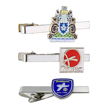 Display of three custom tie clips vertically arranged on white background, featuring various emblem designs including heraldic, abstract, and shield styles with custom text and logos for business customization.