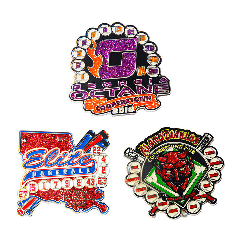 Three custom glitter baseball trading pins showcasing diverse designs including a purple G with orange flames, a red map-shaped pin, and a shield with a green diamond and devil head, all featuring custom team and event text.