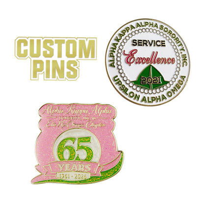 Custom Alpha Kappa Alpha sorority pins, featuring a round Upsilon Alpha Omega 'Service Excellence' pin and a pink glitter 65th anniversary shield pin.