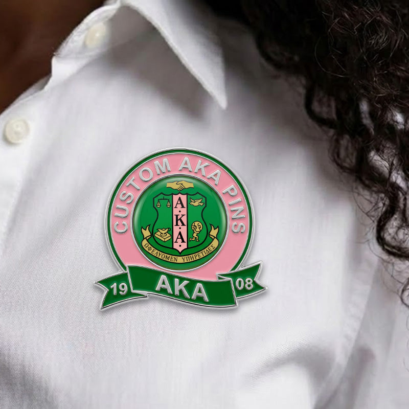 A custom silver-plated AKA sorority pin worn on a white button-down shirt, showcasing its size and realistic look.