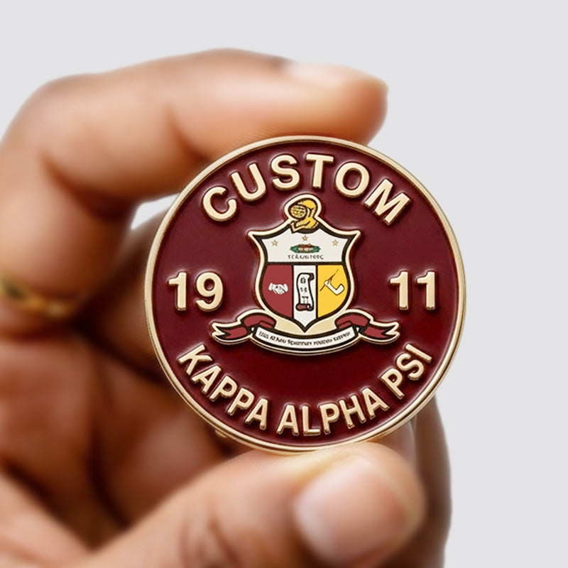 A person's hand holding a custom round Kappa Alpha Psi fraternity pin showing its size, featuring the 1911 founding year and crest.