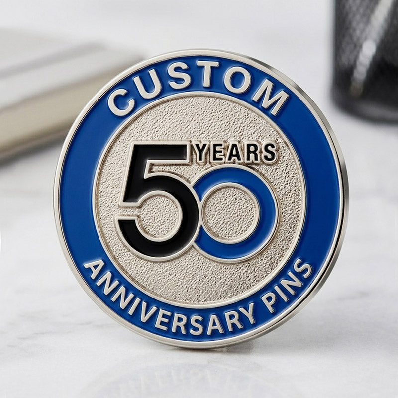 A custom round 50th anniversary lapel pin in silver tone, featuring a textured silver center with a black and blue interlocking 50 design and a royal blue enamel text border.