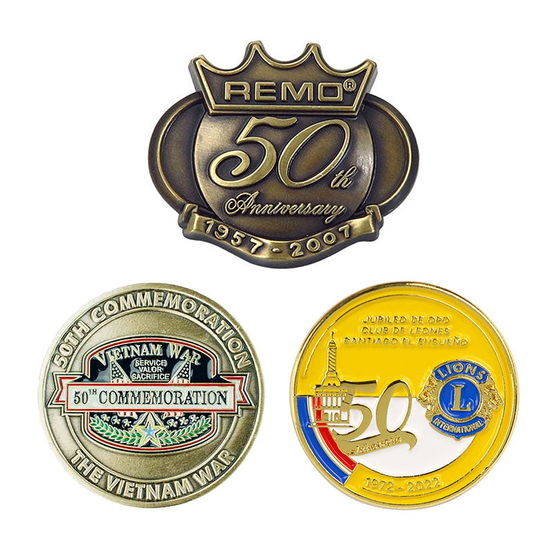 A collection of three custom 50th anniversary pins showcasing an antique bronze crown-shaped pin, a round silver-tone military commemoration token, and a bright yellow enamel Lions International milestone badge.