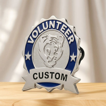 A side-angle perspective view of a custom volunteer service lapel pin in silver tone, displaying a textured silver center with a lion emblem, surrounded by a blue enamel border and a personalized bottom ribbon banner