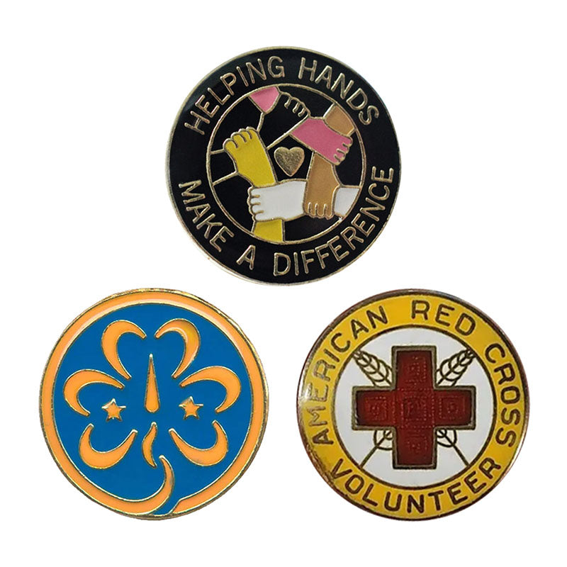 A collection of three round custom volunteer appreciation pins, showcasing a black enamel "Helping Hands" community badge, a blue and orange Girl Scouts trefoil pin, and a yellow-bordered American Red Cross volunteer medal.