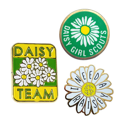 A collection of three unique custom daisy-themed enamel pins, featuring a rectangular green and yellow "Daisy Team" badge, a round green "Daisy Girl Scouts" emblem pin, and a daisy-shaped badge with text