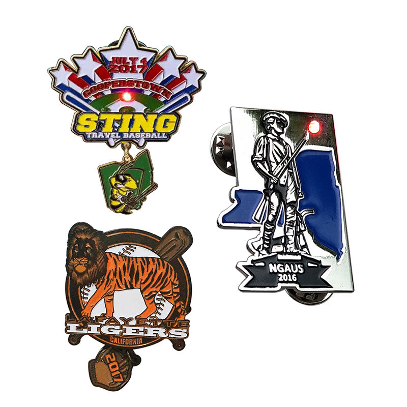 Custom enamel pins collection featuring a blinking LED baseball pin, a military lapel pin with a flashing light, and sports team designs with dangling charms.