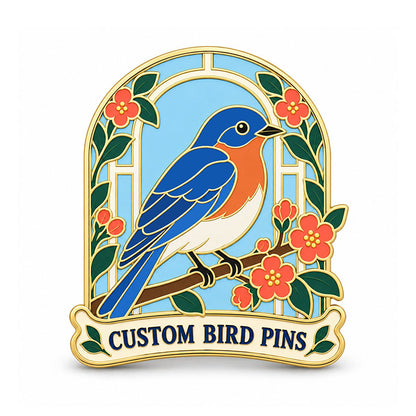 Gold bird pin with a blue and orange songbird framed by blossoms and a pale blue arch