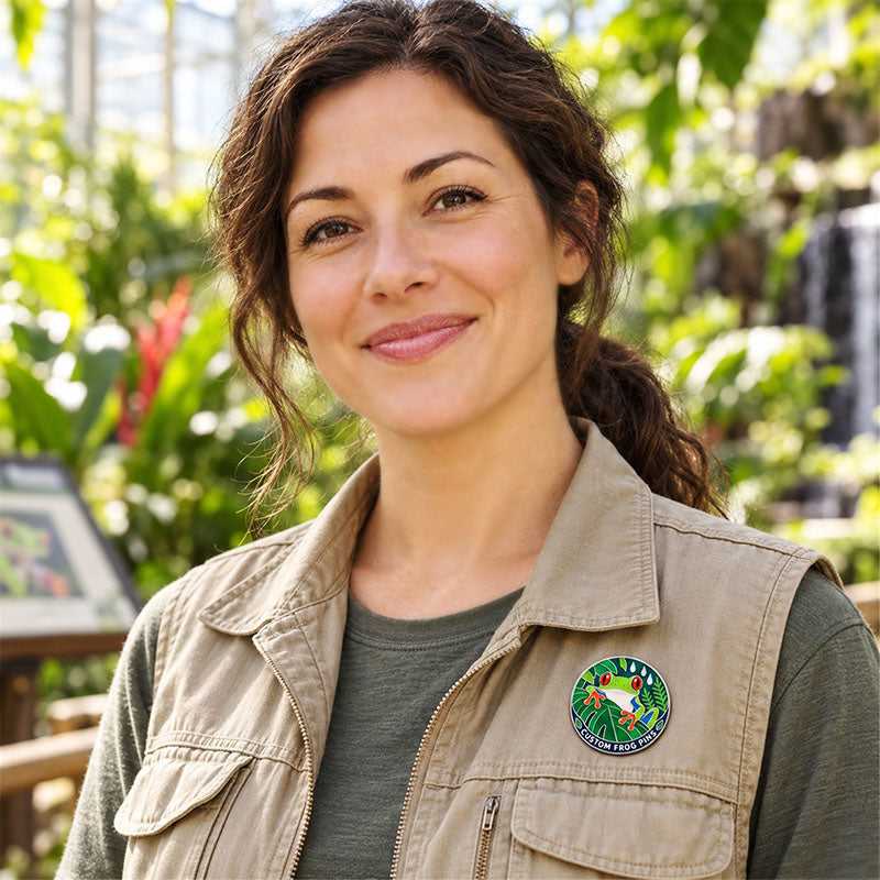 Woman wearing a round tree frog enamel pin on a beige vest surrounded by greenery