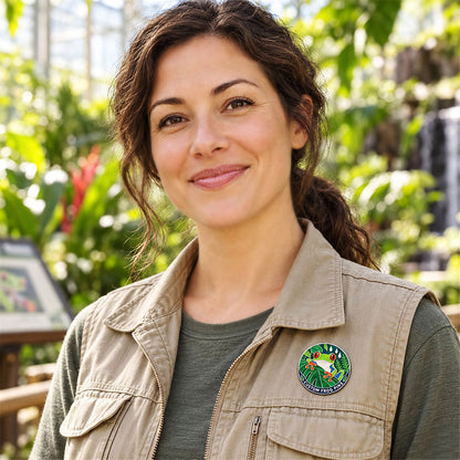 Woman wearing a round tree frog enamel pin on a beige vest surrounded by greenery