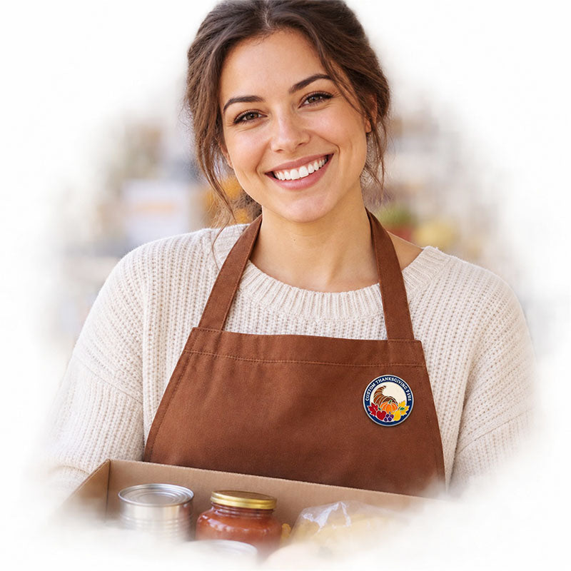 Woman wearing a round Thanksgiving pin on a brown apron while holding food donations