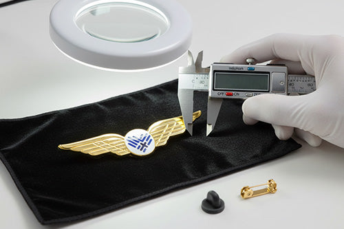 Airline Wing Pins Gold Wings with 3D Embossed Detail Undergoing Precise Measurement with Digital Calipers Alongside Magnifier and Pin Clutch on Black Velvet
