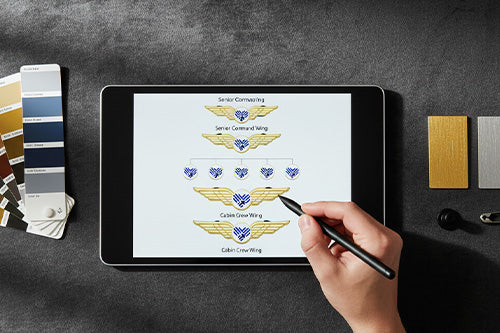 Airline Wing Pins With Designer Using Stylus on Tablet to Present Rank Insignia Hierarchy Featuring Color Swatches and Metal Samples for Custom Aviation Badge Collaboration