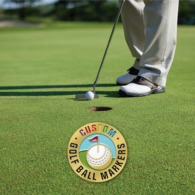 Custom golf ball markers featuring a gold design with text, shown in the foreground with a golfer using a putter on the green in the background.