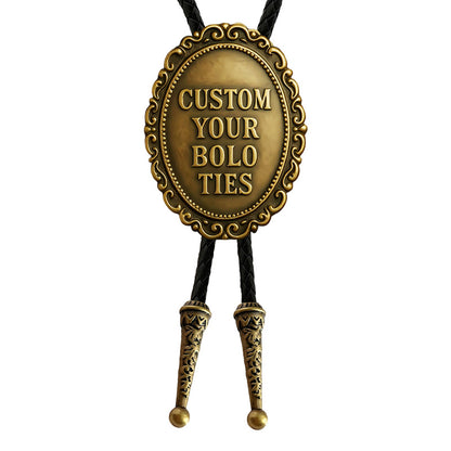 Custom gold bolo tie featuring an oval metal plaque with engraved custom text, intricate decorative patterns, and a black braided cord.
