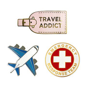 Three travel-themed pins on a white background: 'Travel Addict' tag, airplane, and 'Emergency Response Team' badge.