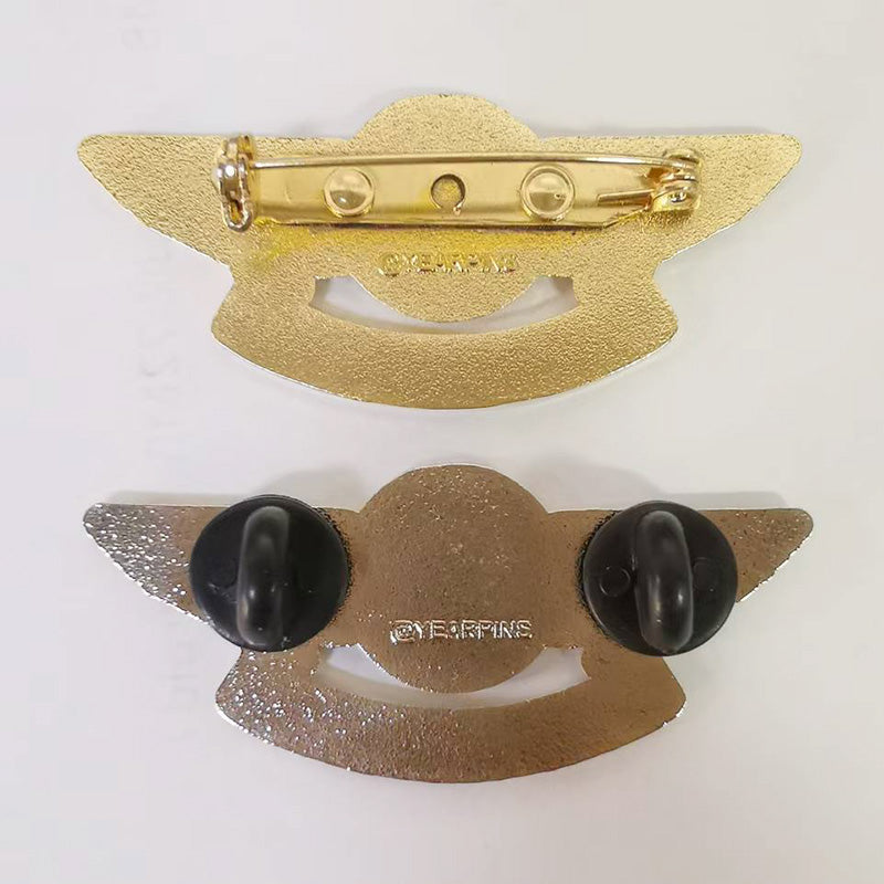 Two gold-tone pilot wings lapel pins displayed back-to-back against a white background — one showing a standard pin-back clasp mechanism with engraved branding, the other featuring dual black rubber clutches attached at the wingtips