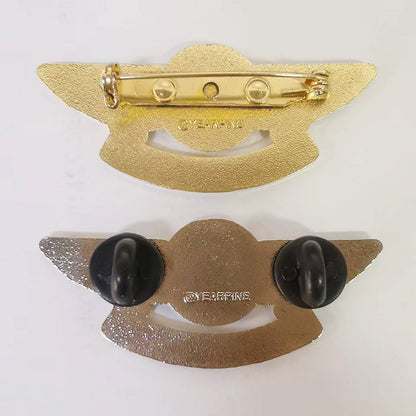 Two gold-tone pilot wings lapel pins displayed back-to-back against a white background — one showing a standard pin-back clasp mechanism with engraved branding, the other featuring dual black rubber clutches attached at the wingtips