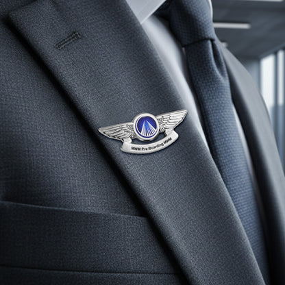 Silver-tone pilot wings lapel pin worn on the lapel of a dark gray suit jacket, featuring a blue circular emblem with a white triangular runway design and a silver banner below inscribed with “MWM Pre-Boarding 1988” — displayed against a softly blurred indoor background with natural light.