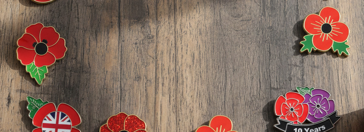 Poppy Pins Showcasing A Collection Of Red Poppy Flower Badges With Glossy And Sparkle Finishes Black Centers And Green Leaves Featuring Custom Text Including The Salvation Army Matt Owen And 10 Years Arranged On A Wooden Desktop For Commemoration And Recognition
