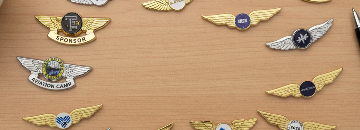 Pilot Wings Pins in Gold and Silver Finishes Showcasing A Collection of Winged Badge Designs Featuring Custom Text Including Sponsor, Elevate, Amen, and Camp Years on Wooden Desktop Display for Event Commemoration And Brand Sponsorship Recognition
